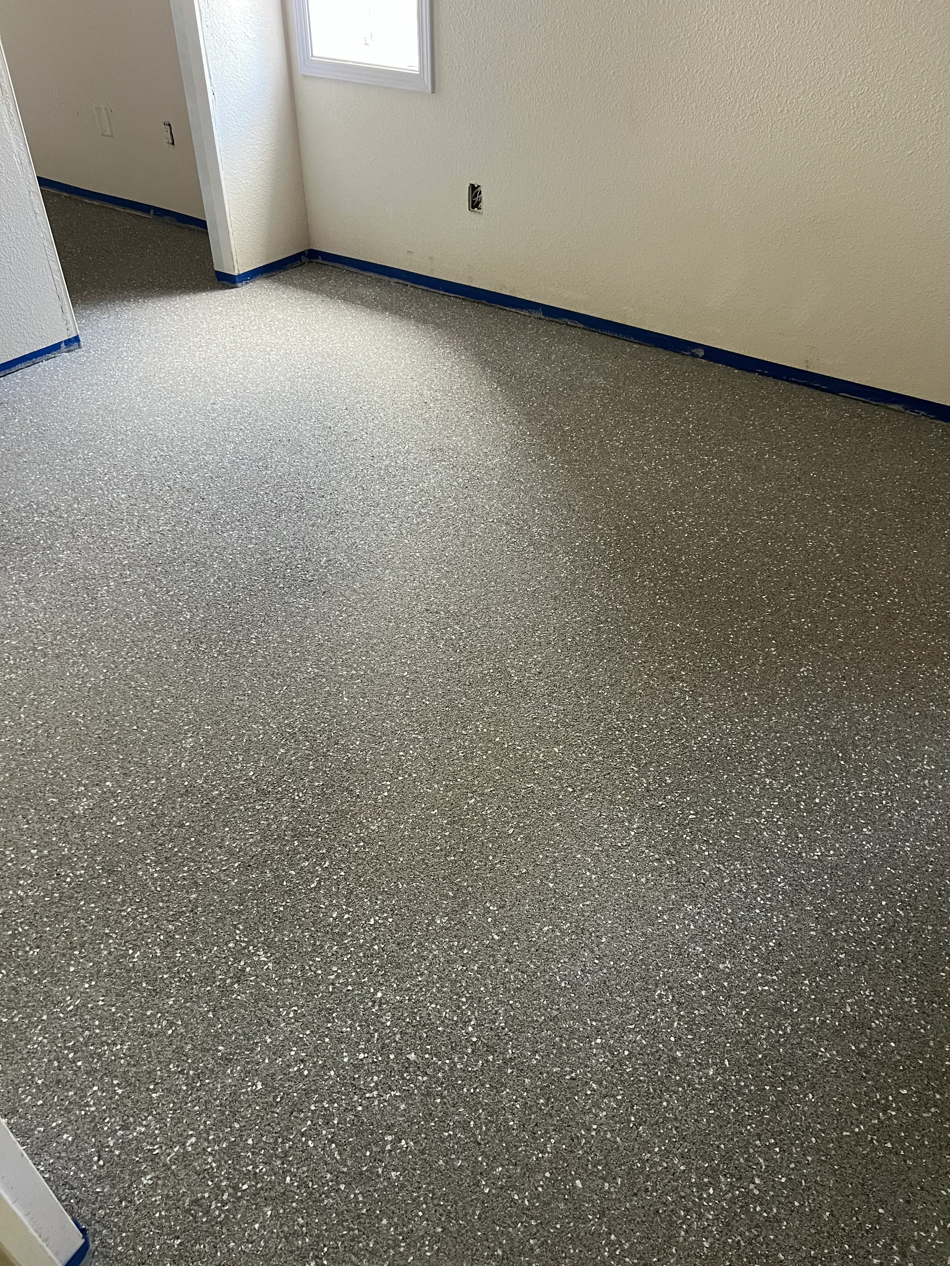 Gray speckled epoxy garage floor with blue trim tape and white wall transition