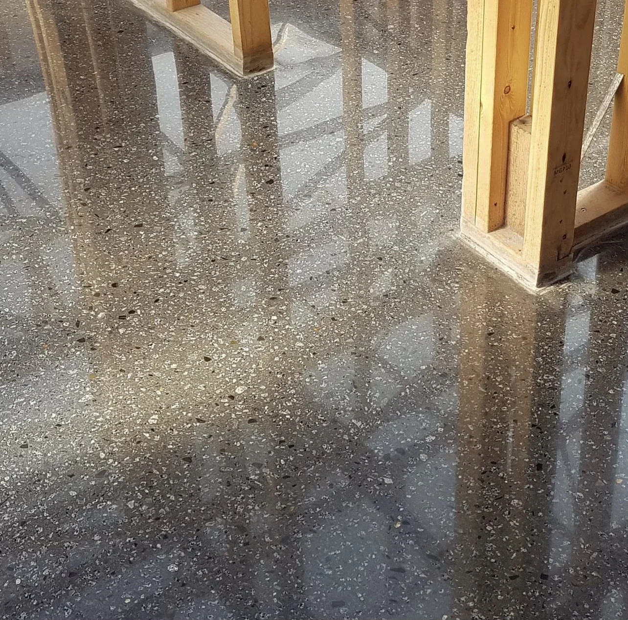 Polished concrete floor with reflective finish and exposed aggregate, wooden framing visible